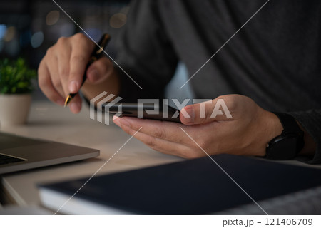 Businessman using a smartphone while holding a pen, multitasking between mobile communication and planning. Suitable for business, productivity, multitasking 121406709