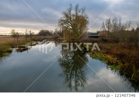 A tree gives a beautiful reflection in a river. A dark sky with clouds in the background A tree gives a beautiful reflection in a river. A dark sky with clouds in the background 121407346