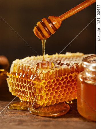 Harvesting Fresh Honeycomb in a Warm Kitchen, Showcasing Golden Honey Dripping From the Wax Cells, Wooden honey dipper 121408485