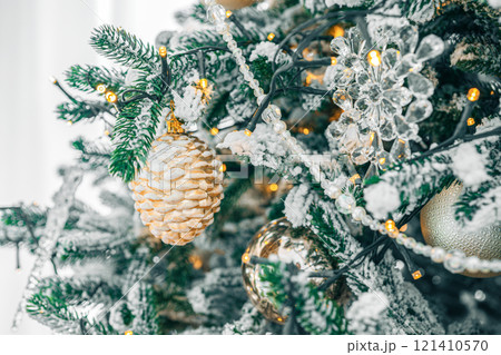 Snowy Christmas tree branch with festive lights and decorative gold and silver ornaments close up Snowy Christmas tree branch with festive lights and decorative gold and silver ornaments close up 121410570