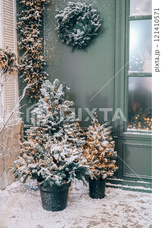 Two small Christmas trees decorated with garlands of sparkling lights with snow on cozy entrance 121410571