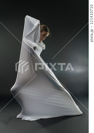 Elegant figure draped in flowing white fabric creates a stunning visual effect 121410710