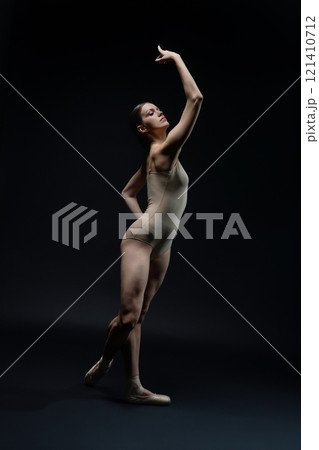 Elegant ballet dancer poses dramatically in a dark studio setting Elegant ballet dancer poses dramatically in a dark studio setting 121410712