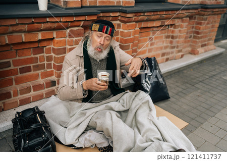 Happy elderly homeless man warming up with cup of coffee on cold urban street, evoking sadness and highlighting issue of homelessness in America. Concept of raw reality of poverty and despair. 121411737