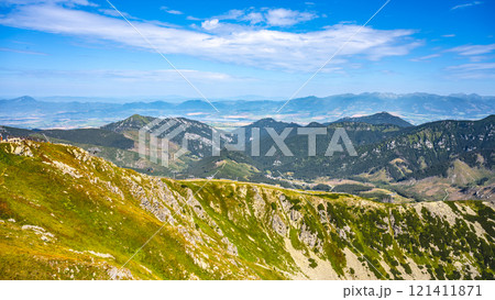 The rolling hills and rugged peaks of Low Tatras National Park rise majestically under a clear blue sky. Lush greenery blankets the slopes, inviting hikers to explore the stunning landscape in summer. 121411871