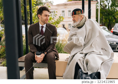 Empathetic businessman in suit listening story of old homeless man sitting on bench, representing growing gap between rich and poor in society. Concept of social issues and economic disparity. 121411965