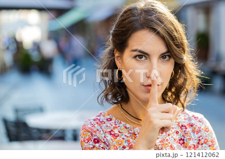 Young woman presses finger to lips makes silence hush sign do not tells gossip secret quiet in city Young woman presses finger to lips makes silence hush sign do not tells gossip secret quiet in city 121412062