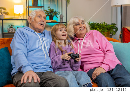 Child girl granddaughter grandparents using joystick controller playing console videogame at home 121412113