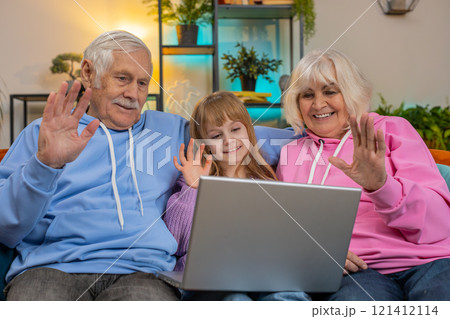 Grandfather grandmother and child granddaughter making video call online on laptop at home sofa 121412114