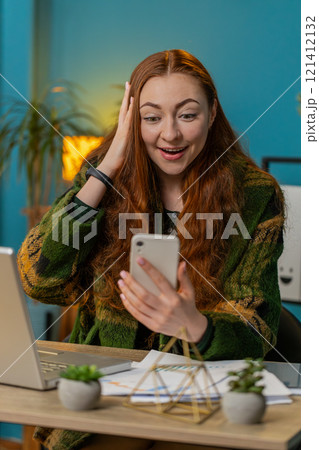 Excited woman at home table use smartphone typing browsing say wow yes found out great big win Excited woman at home table use smartphone typing browsing say wow yes found out great big win 121412132