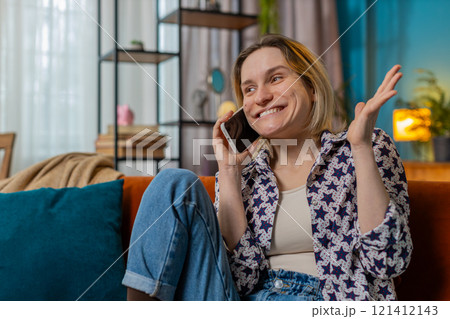 Happy young Caucasian woman making mobile phone conversation with friends sitting on couch at home Happy young Caucasian woman making mobile phone conversation with friends sitting on couch at home 121412143