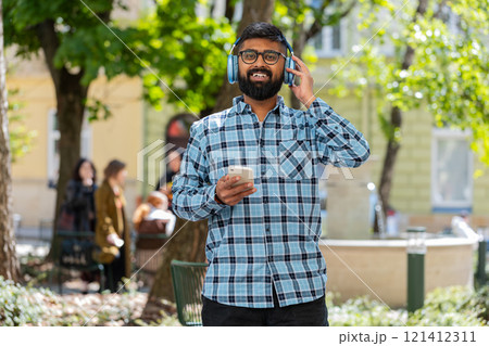 Happy Indian man dancing in wireless headphones listening favorite energetic music on city street 121412311