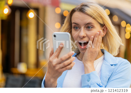 Excited happy winner woman use smartphone looking amazed at screen celebrating win good message news Excited happy winner woman use smartphone looking amazed at screen celebrating win good message news 121412319