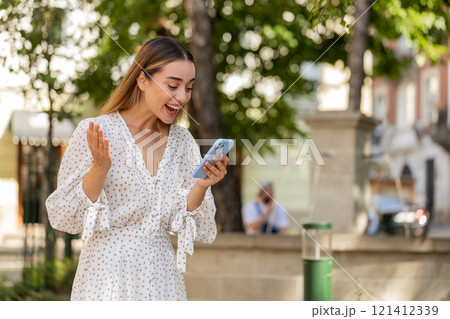 Excited happy woman using smartphone celebrating win receive good message news in urban street 121412339