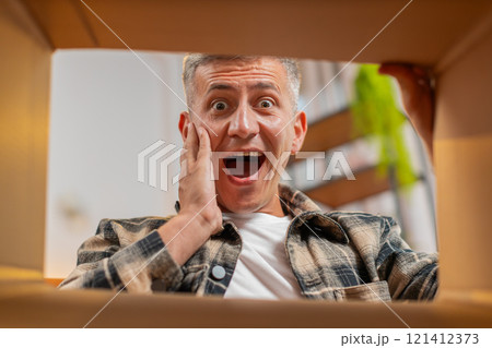 Happy smiling man shopper unpacking cardboard box delivery parcel online shopping purchase at home 121412373