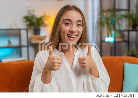 Portrait of excited smiling young woman showing double thumbs up sitting on sofa couch at home Portrait of excited smiling young woman showing double thumbs up sitting on sofa couch at home 121412381