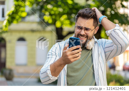 Upset young man using smartphone typing browsing, loses becoming shocked bad news on city street 121412401