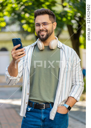 Smiling young man using smartphone typing texting scrolling social media app on city town street 121412402