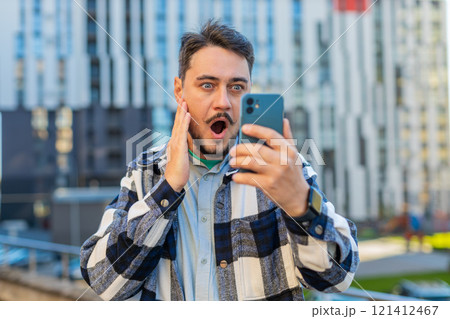 Caucasian mature man looking shocked while reading good news on smartphone in downtown city street Caucasian mature man looking shocked while reading good news on smartphone in downtown city street 121412467