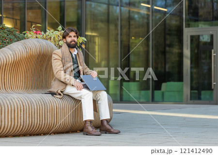 Indian man freelancer sitting on city street closes laptop finishing working online distant job Indian man freelancer sitting on city street closes laptop finishing working online distant job 121412490