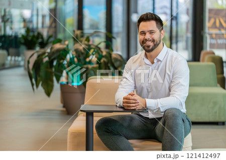 Portrait of smiling young businessman looking at camera sitting in hotel lobby Portrait of smiling young businessman looking at camera sitting in hotel lobby 121412497