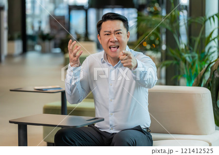 Angry mature boss arguing over video call looking at camera sitting at modern workplace in office 121412525