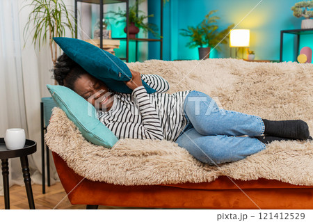 African American woman lying on sofa closing eyes covering face with pillow feeling migraine pain African American woman lying on sofa closing eyes covering face with pillow feeling migraine pain 121412529