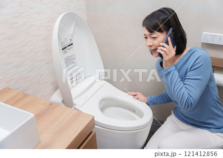 トイレのトラブルで水道業者に電話する女性 トイレのトラブルで水道業者に電話する女性 121412856