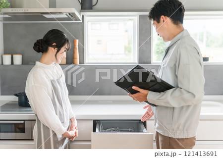キッチンで水道屋・設備屋に食洗機・食器洗浄器の説明を受ける主婦の女性 121413691