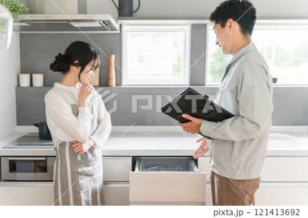 キッチンで水道屋・設備屋に食洗機・食器洗浄器の説明を受ける主婦の女性 キッチンで水道屋・設備屋に食洗機・食器洗浄器の説明を受ける主婦の女性 121413692
