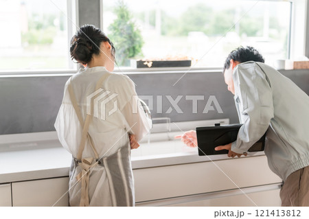 キッチンで水道屋・設備屋の説明を受ける主婦の女性 キッチンで水道屋・設備屋の説明を受ける主婦の女性 121413812