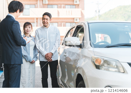 自動車購入・査定・買取にきた夫婦と接客するセールスマンの若いアジア人男性 121414606