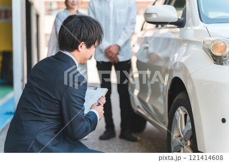 自動車購入・査定・買取にきた夫婦を接客するセールスマンの若いアジア人男性 自動車購入・査定・買取にきた夫婦を接客するセールスマンの若いアジア人男性 121414608
