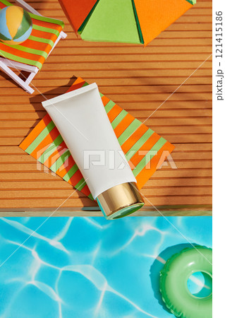 A white tube mockup was positioned on a paper mat, with a chair, a ball, and a paper parasol on a brown-striped surface. A swimming pool background is ideal for ads promoting sunscreen. Overhead view. 121415186