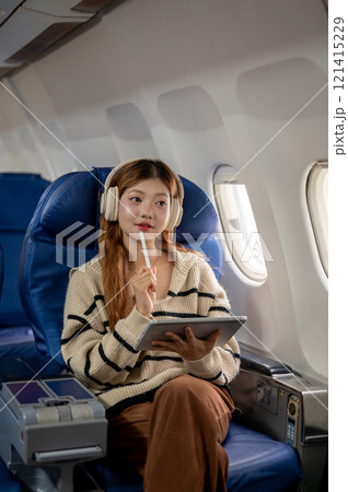 Charming Asian woman gazes at the sky view from the window while using her tablet during the flight. Charming Asian woman gazes at the sky view from the window while using her tablet during the flight. 121415229