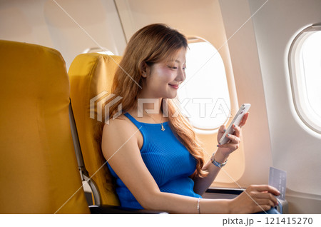 A pretty, happy Asian female passenger uses her smartphone to read a chat during the flight. A pretty, happy Asian female passenger uses her smartphone to read a chat during the flight. 121415270