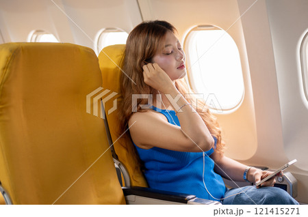 Attractive, calm Asian female passenger puts on her earphones, listening to music during the flight. Attractive, calm Asian female passenger puts on her earphones, listening to music during the flight. 121415271