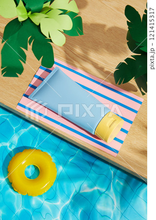 Sunscreen ads use the concept of a miniature pool. A blue tube replica was set on a pink paper mat with a palm tree on a wooden platform, while an inflatable ring floated on the water. High angle. 121415317