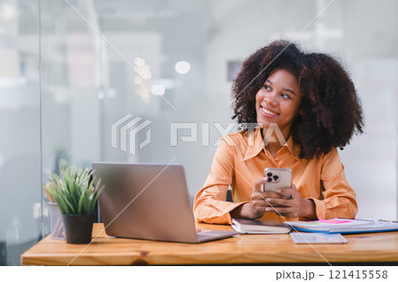 African American Woman Smiling Using Smartphone at Desk. 121415558