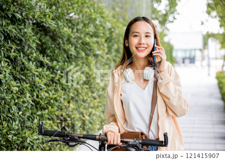 Asian young woman walking in countryside outdoor with her bicycle she using mobile phone talking with friend, Happy female stand on city street with bike using smartphone for summer sightseeing walk Asian young woman walking in countryside outdoor with her bicycle she using mobile phone talking with friend, Happy female stand on city street with bike using smartphone for summer sightseeing walk 121415907