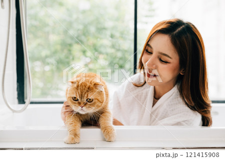 A woman's bathroom retreat includes quality time with her Scottish Fold cat in the tub, portraying the joy of owner-pet love and happiness. 121415908