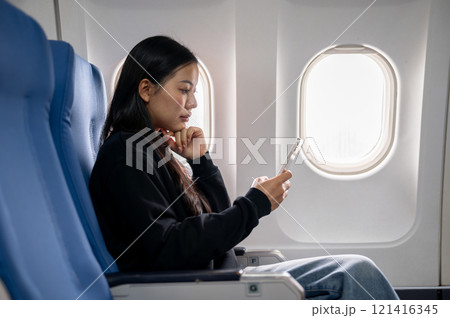 A side view of a relaxed Asian female passenger reading messages on her smartphone during the flight 121416345