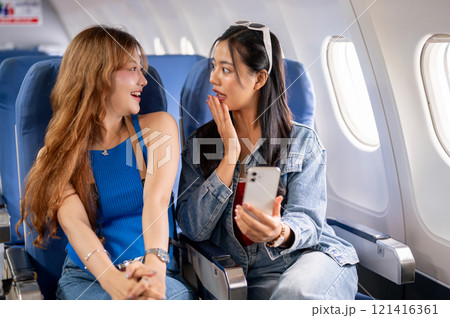 Two happy Asian females traveling on vacation together, enjoying a conversation during the flight. 121416361