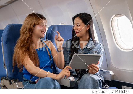 Two cheerful Asian women watch a video on a tablet and enjoy a conversation during the flight. Two cheerful Asian women watch a video on a tablet and enjoy a conversation during the flight. 121416379