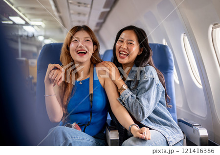 Two joyful Asian female friends, excited for their vacation, sit on a plane with happy expressions. Two joyful Asian female friends, excited for their vacation, sit on a plane with happy expressions. 121416386