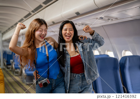 Two excited, joyful Asian female best friends stand in the aisle of a plane, traveling together. Two excited, joyful Asian female best friends stand in the aisle of a plane, traveling together. 121416392