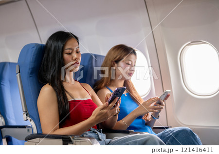 Two Asian women are individually using their smartphones during the flight, traveling to somewhere. Two Asian women are individually using their smartphones during the flight, traveling to somewhere. 121416411