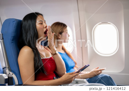 A tired Asian female passenger covers her mouth while yawning, feeling sleepy during the long flight A tired Asian female passenger covers her mouth while yawning, feeling sleepy during the long flight 121416412