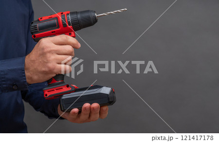 a man installs a battery in a screwdriver. close-up on a gray background. copy space a man installs a battery in a screwdriver. close-up on a gray background. copy space 121417178