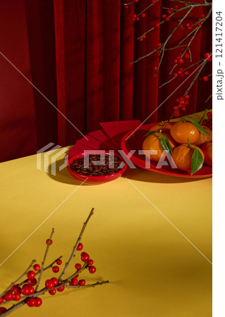 High angle shot photograph on yellow table top, which displaying many Tet's theme items like roasted watermelon seed, fresh fruits and decorative flower. Red curtain on red background High angle shot photograph on yellow table top, which displaying many Tet's theme items like roasted watermelon seed, fresh fruits and decorative flower. Red curtain on red background 121417204
